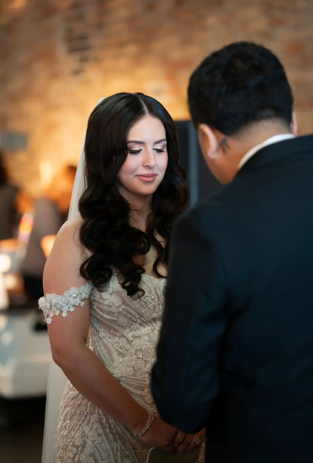Bride with soft glam makeup, dark romantic waves, and a veil during her wedding ceremony